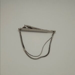 vintage tie clip or tie bar with a safety chain, often styled in silver